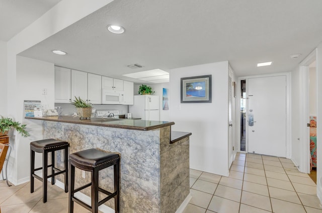 291 Scenic Gulf Dr Unit 400, Miramar Beach, FL 32550 - kitchen with white appliances, light tile patterned flooring, a breakfast bar area, a peninsula, and white cabinets