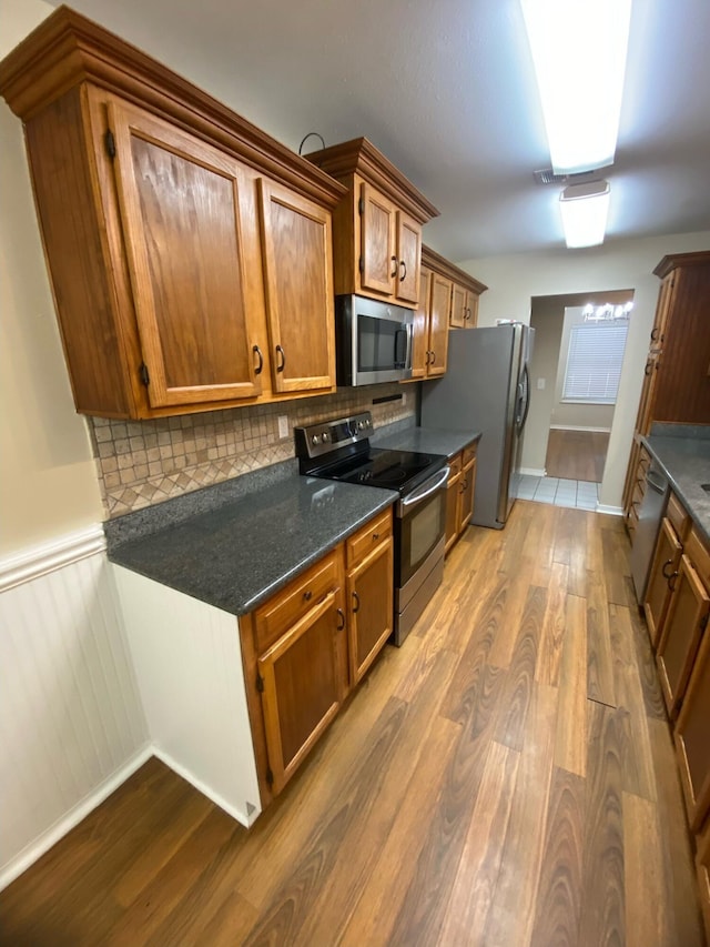 64 Hampton Cir, Niceville, FL 32578 - kitchen featuring stainless steel appliances, wood finished floors, brown cabinetry, tasteful backsplash, and wainscoting