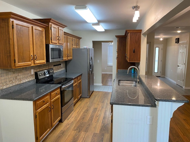 64 Hampton Cir, Niceville, FL 32578 - kitchen with stainless steel appliances, decorative backsplash, brown cabinetry, light wood-type flooring, and dark stone countertops