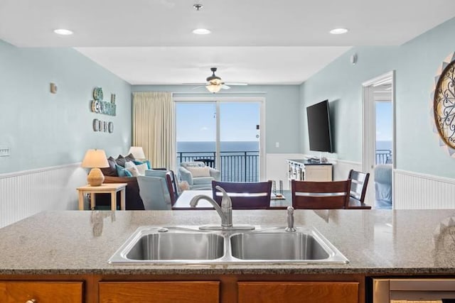 16701 Front Beach Rd Unit 1807, Panama City Beach, FL 32413 - kitchen with brown cabinetry, wainscoting, open floor plan, ceiling fan, and stone counters