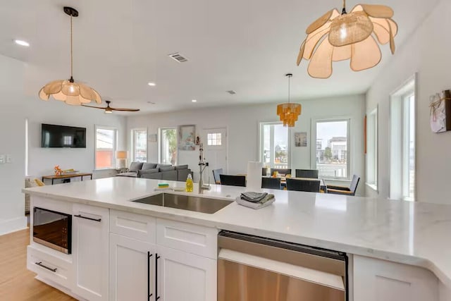 7411 Grand Navarre Blvd, Navarre, FL 32566 - kitchen with stainless steel dishwasher, open floor plan, white cabinets, decorative light fixtures, and ceiling fan