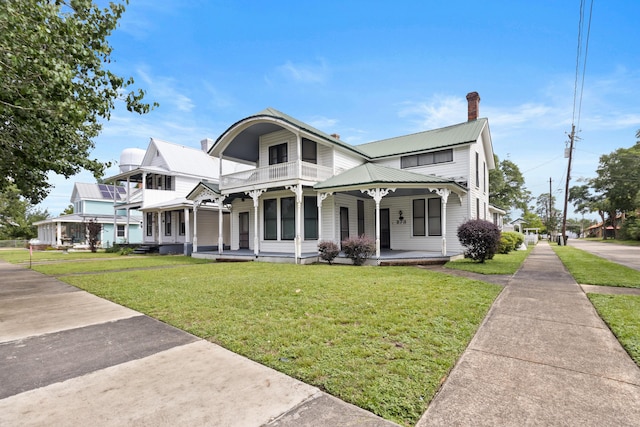 273 E Live Oak Ave, Defuniak Springs, FL 32435 - victorian home featuring a porch, a chimney, a metal roof, a balcony, and a front yard