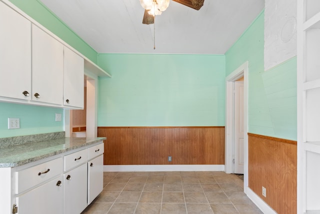 273 E Live Oak Ave, Defuniak Springs, FL 32435 - kitchen with wainscoting, a ceiling fan, wooden walls, white cabinets, and light stone counters