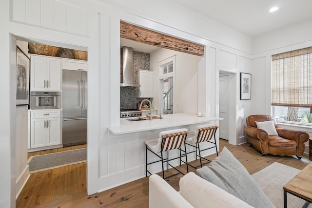 58 Pine Needle Way, Santa Rosa Beach, FL 32459 - kitchen featuring stainless steel built in fridge, wall chimney range hood, white cabinets, wood finished floors, and a kitchen breakfast bar