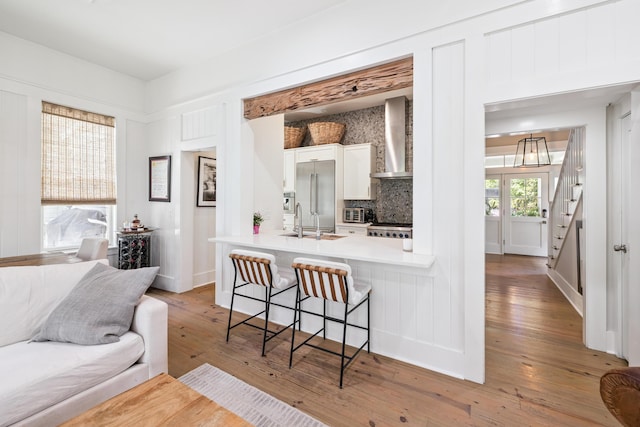 58 Pine Needle Way, Santa Rosa Beach, FL 32459 - kitchen with wall chimney exhaust hood, high end fridge, a breakfast bar, wood-type flooring, and white cabinetry