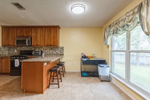 527 Tom Sawyer Ln, Crestview, FL 32536 - kitchen with stainless steel microwave, black gas range, brown cabinets, a breakfast bar, and tasteful backsplash