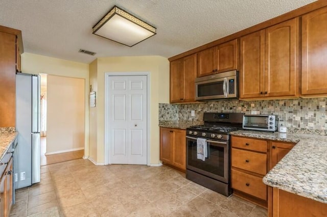 527 Tom Sawyer Ln, Crestview, FL 32536 - kitchen with appliances with stainless steel finishes, brown cabinets, decorative backsplash, and a textured ceiling