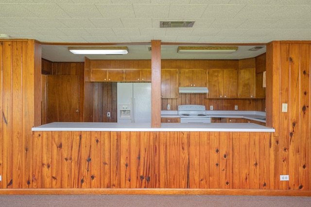 942 Varnum Rd, Laurel Hill, FL 32567 - kitchen with white appliances, under cabinet range hood, brown cabinetry, wood walls, and a peninsula