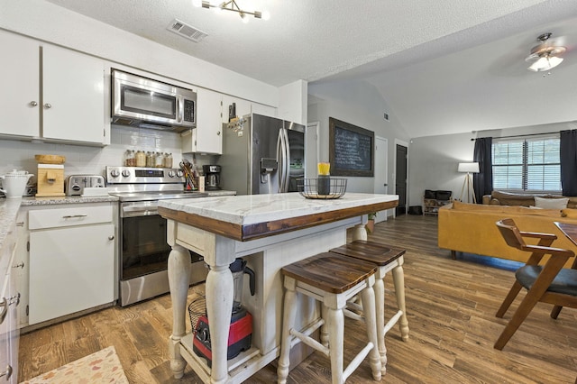 3774 Laird Rd, Crestview, FL 32539 - kitchen featuring stainless steel appliances, vaulted ceiling, white cabinetry, wood finished floors, and open floor plan