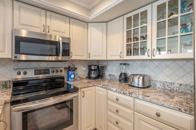 100 Gulf Shore Dr Unit 305, Destin, FL 32541 - kitchen with appliances with stainless steel finishes, crown molding, tasteful backsplash, white cabinetry, and glass insert cabinets