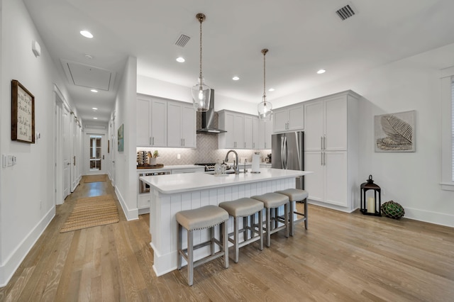 22 Cypress Rdg, Santa Rosa Beach, FL 32459 - kitchen featuring wall chimney exhaust hood, a breakfast bar, an island with sink, light wood-style floors, and backsplash