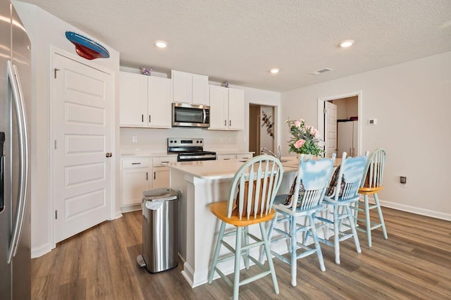 4649 Naval Ct, Crestview, FL 32539 - kitchen with appliances with stainless steel finishes, dark wood-type flooring, a center island with sink, light countertops, and a breakfast bar area