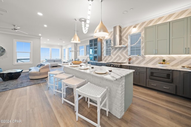 19989 Front Beach Rd, Panama City Beach, FL 32413 - kitchen featuring wall chimney exhaust hood, crown molding, stainless steel microwave, light wood-style flooring, and a breakfast bar area