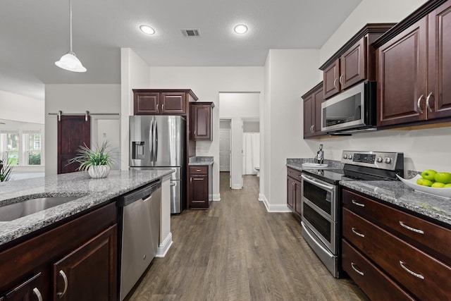 8152 Nevada St, Navarre, FL 32566 - kitchen featuring appliances with stainless steel finishes, dark wood-style floors, light stone countertops, hanging light fixtures, and a barn door