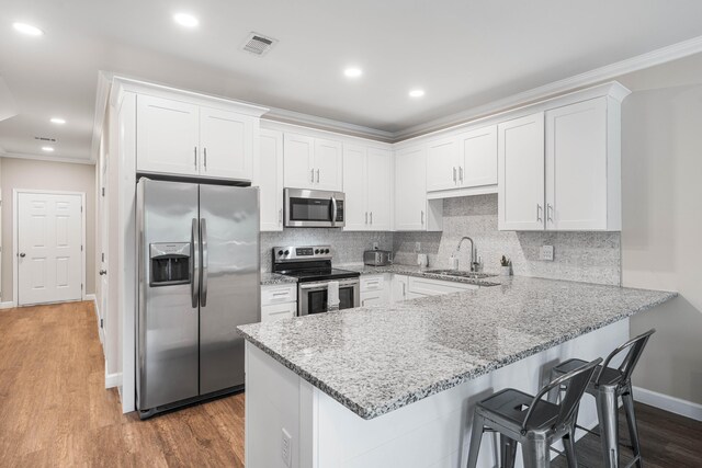 1819 Stable Ln, Fort Walton Beach, FL 32547 - kitchen featuring appliances with stainless steel finishes, a peninsula, white cabinetry, ornamental molding, and a kitchen breakfast bar