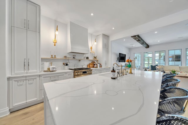 34 E Surfside Dr, Santa Rosa Beach, FL 32459 - kitchen with premium range hood, open floor plan, high end stainless steel range, light wood finished floors, and a kitchen bar