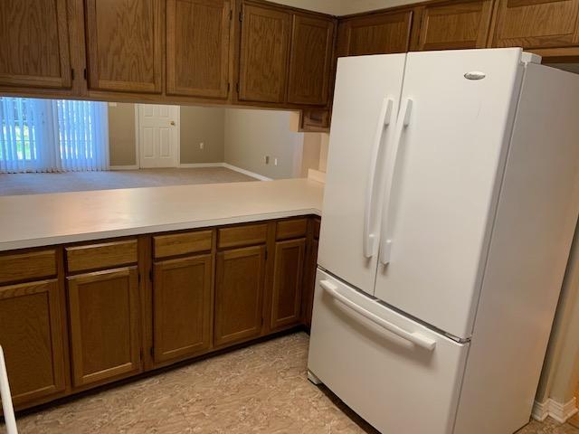 507 Chinas Cv Unit C, Fort Walton Beach, FL 32547 - kitchen with freestanding refrigerator, light countertops, brown cabinetry, and a peninsula