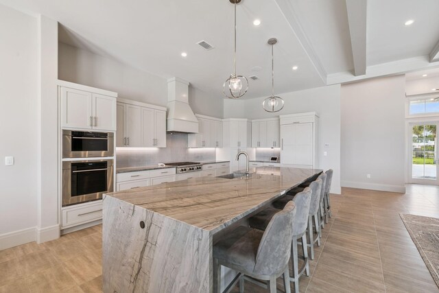 31 Driftwood Ct, Santa Rosa Beach, FL 32459 - kitchen featuring custom range hood, backsplash, stainless steel appliances, a large island with sink, and light stone counters
