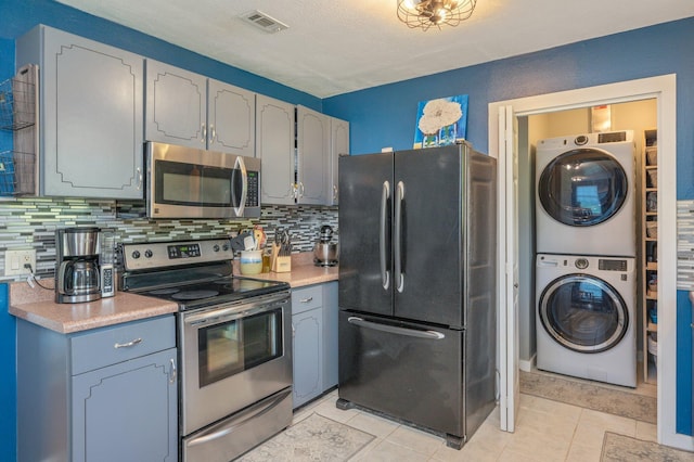 5358 Cox Ln, Crestview, FL 32539 - kitchen with appliances with stainless steel finishes, stacked washing machine and dryer, tasteful backsplash, light countertops, and light tile patterned flooring