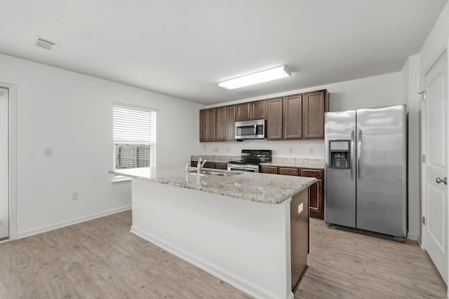 718 Widgeon Way, Crestview, FL 32539 - kitchen featuring stainless steel appliances, light wood-type flooring, dark brown cabinetry, an island with sink, and light stone countertops