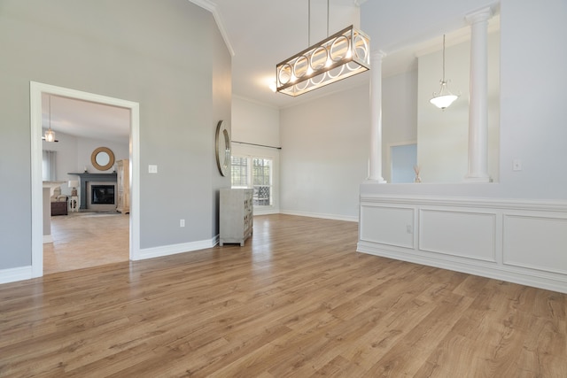180 Gulf Pines Ct, Freeport, FL 32439 - unfurnished living room with crown molding, light wood-style flooring, a towering ceiling, decorative columns, and a fireplace with raised hearth