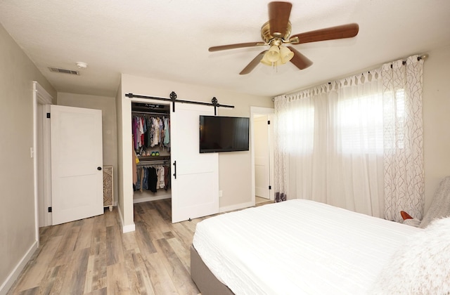 52 NE Iowa Dr, Fort Walton Beach, FL 32548 - bedroom with light wood finished floors, a walk in closet, a barn door, a closet, and a ceiling fan