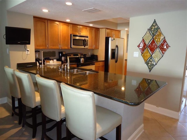 291 Scenic Gulf Dr Unit 1401, Miramar Beach, FL 32550 - kitchen with appliances with stainless steel finishes, recessed lighting, a peninsula, dark stone counters, and brown cabinetry
