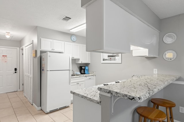 134 Damon Cir Unit Q, Panama City Beach, FL 32407 - kitchen with white appliances, a peninsula, a breakfast bar, light tile patterned floors, and white cabinetry