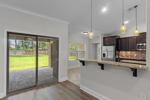 7478 Brevard St, Navarre, FL 32566 - kitchen with stainless steel appliances, a kitchen breakfast bar, crown molding, dark brown cabinets, and light stone counters
