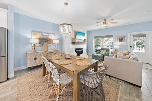 115 N Barcelona Ave, Santa Rosa Beach, FL 32459 - dining space with a fireplace, a ceiling fan, light wood-style floors, and a chandelier