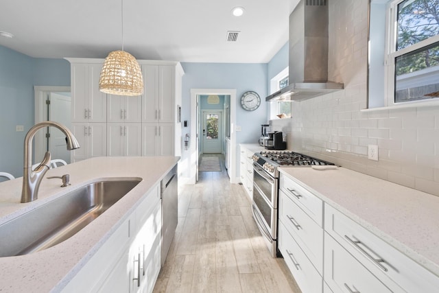 115 N Barcelona Ave, Santa Rosa Beach, FL 32459 - kitchen with stainless steel appliances, wall chimney exhaust hood, white cabinets, tasteful backsplash, and hanging light fixtures