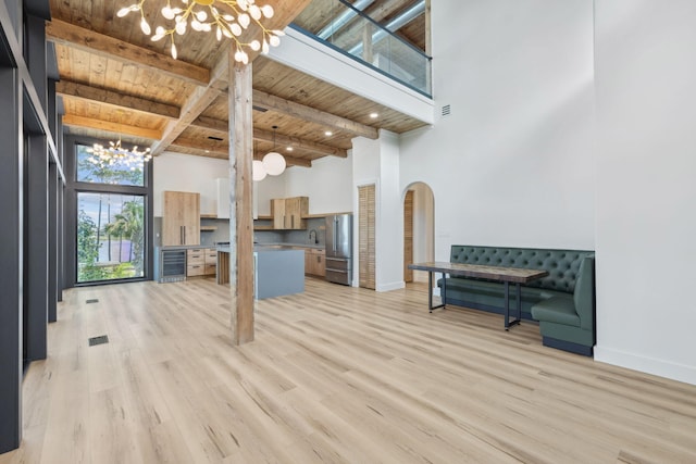 129 Oyster Lake Dr, Santa Rosa Beach, FL 32459 - unfurnished living room featuring a chandelier, a wood ceiling with exposed beams, beverage cooler, arched walkways, and a towering ceiling