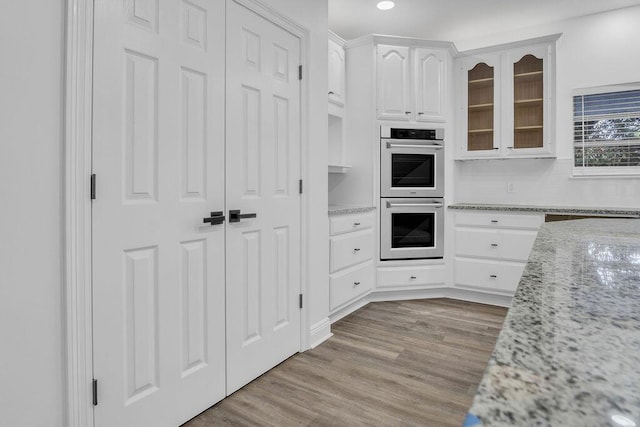 1005 Shalimar Point Dr, Shalimar, FL 32579 - kitchen featuring stainless steel double oven, white cabinets, glass insert cabinets, light wood-style flooring, and light stone countertops