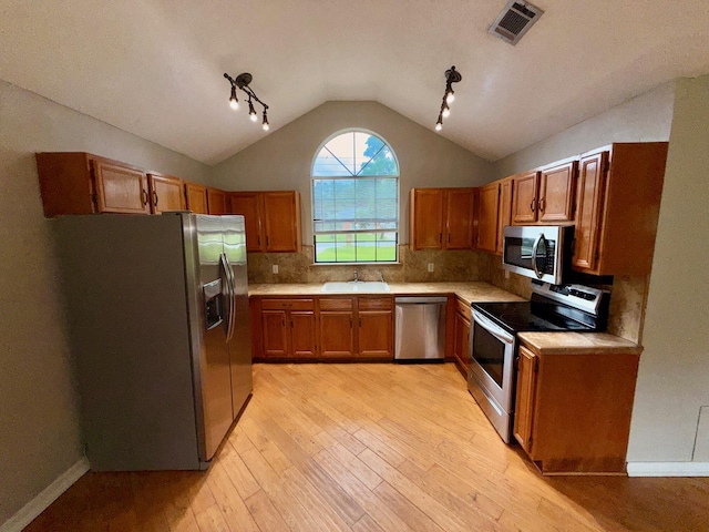 7167 Manatee St, Navarre, FL 32566 - kitchen featuring appliances with stainless steel finishes, brown cabinets, light wood finished floors, lofted ceiling, and light countertops
