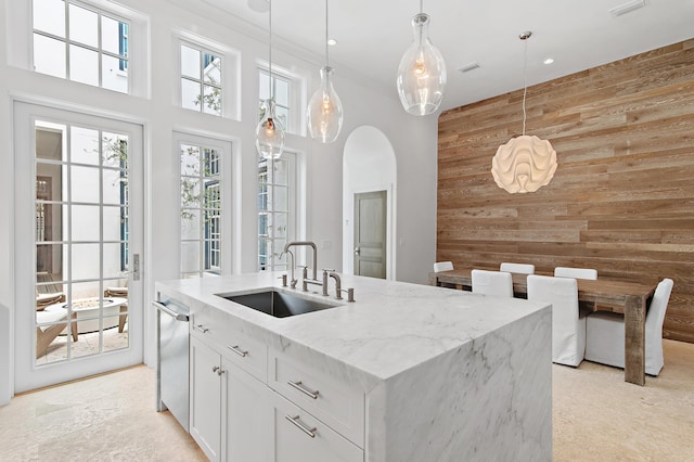 37 Sugar Loaf Aly, Alys Beach, FL 32461 - kitchen with an accent wall, wooden walls, white cabinetry, light stone countertops, and a kitchen island with sink