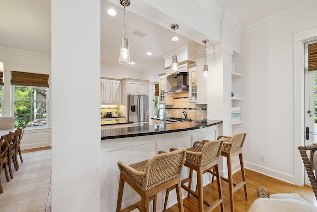 9 W Salt Box Ln, Watersound, FL 32461 - kitchen with stainless steel refrigerator with ice dispenser, wall chimney exhaust hood, ornamental molding, glass insert cabinets, and light wood finished floors