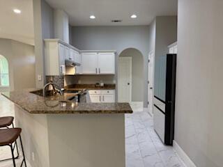 4906 Laurel Oak Dr, Pace, FL 32571 - kitchen with arched walkways, a peninsula, dark stone countertops, a kitchen bar, and recessed lighting