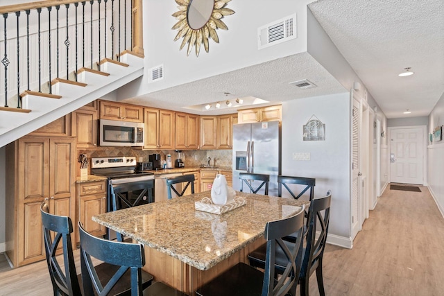 3290 Scenic Highway 98 Unit 305B, Destin, FL 32541 - kitchen featuring stainless steel appliances, a textured ceiling, light wood-type flooring, a breakfast bar, and light stone countertops