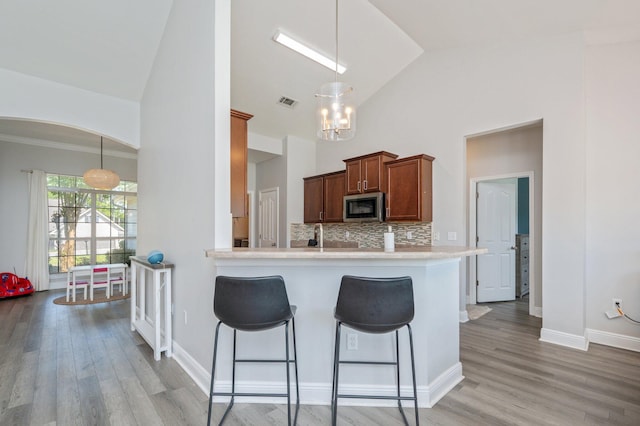 138 Crab Apple Ave, Crestview, FL 32536 - kitchen with stainless steel microwave, a kitchen breakfast bar, high vaulted ceiling, tasteful backsplash, and light wood-style floors