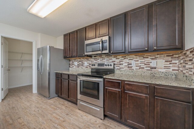 728 Widgeon Way, Crestview, FL 32539 - kitchen with appliances with stainless steel finishes, light wood finished floors, backsplash, dark brown cabinetry, and light stone countertops