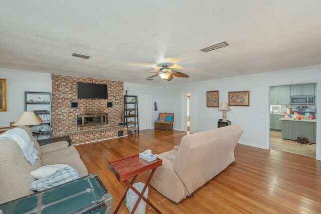 22 James Ave, Shalimar, FL 32579 - living room featuring light wood finished floors, ceiling fan, a textured ceiling, a brick fireplace, and crown molding