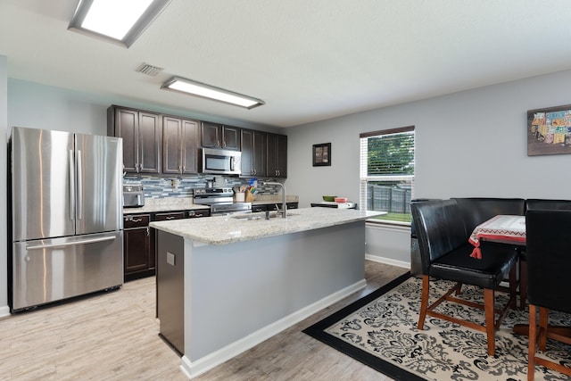 4605 Plover Dr, Crestview, FL 32539 - kitchen featuring stainless steel appliances, dark brown cabinets, light wood-style floors, tasteful backsplash, and a center island with sink
