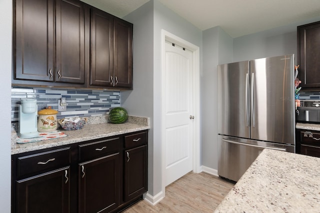 4605 Plover Dr, Crestview, FL 32539 - kitchen featuring freestanding refrigerator, decorative backsplash, light wood finished floors, dark brown cabinetry, and light stone counters