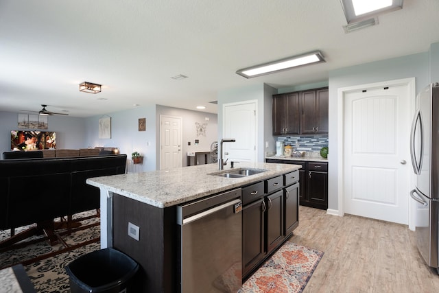 4605 Plover Dr, Crestview, FL 32539 - kitchen featuring stainless steel appliances, light wood-type flooring, a center island with sink, dark brown cabinets, and light stone countertops