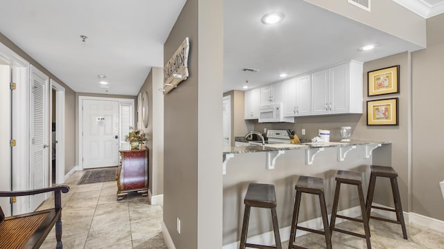 6415 Thomas Dr Unit 1205, Panama City Beach, FL 32408 - kitchen featuring white appliances, light stone countertops, white cabinetry, a kitchen bar, and recessed lighting