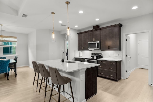 8450 Dreams Float Ct, Panama City Beach, FL 32413 - kitchen with appliances with stainless steel finishes, light wood-style flooring, a kitchen bar, tasteful backsplash, and dark brown cabinetry