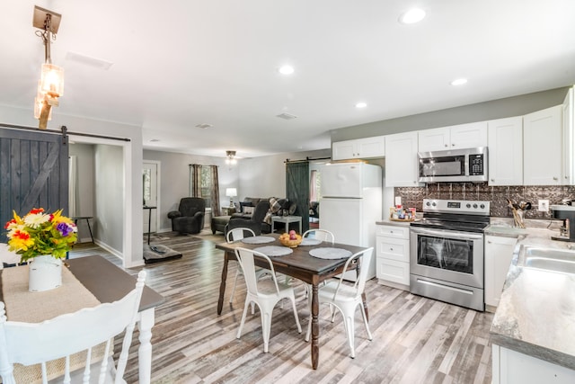 2141 C Shelby Ln, Westville, FL 32464 - kitchen featuring a barn door, appliances with stainless steel finishes, light wood-style flooring, white cabinets, and decorative backsplash