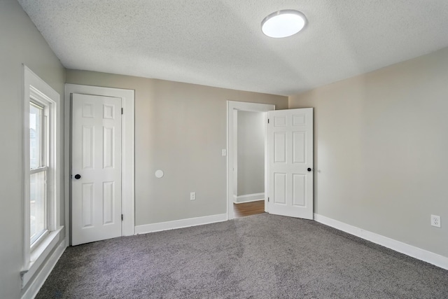 unfurnished bedroom featuring multiple windows, dark colored carpet, and a textured ceiling