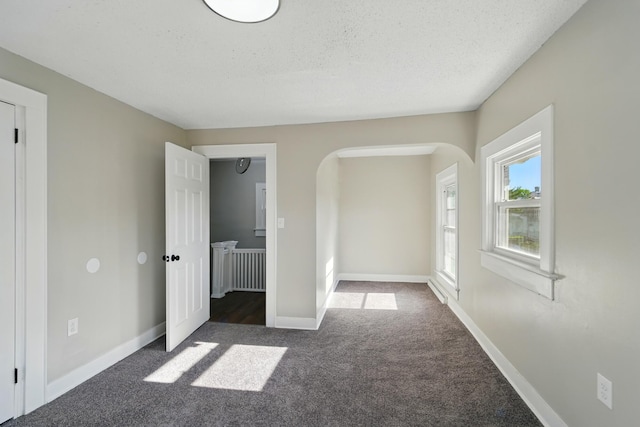 unfurnished bedroom with arched walkways, baseboards, dark carpet, and a textured ceiling