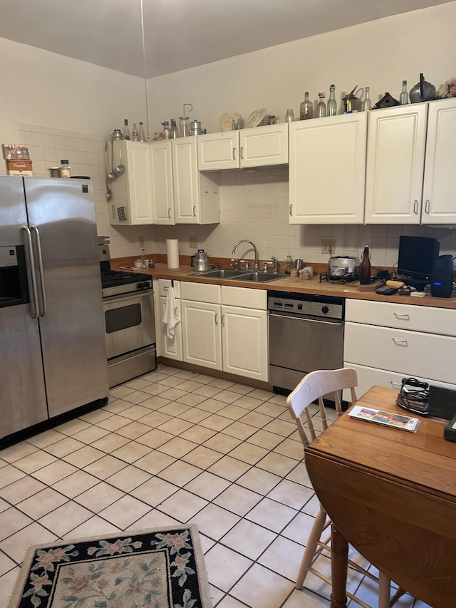 kitchen with sink, tasteful backsplash, white cabinetry, light tile patterned floors, and appliances with stainless steel finishes